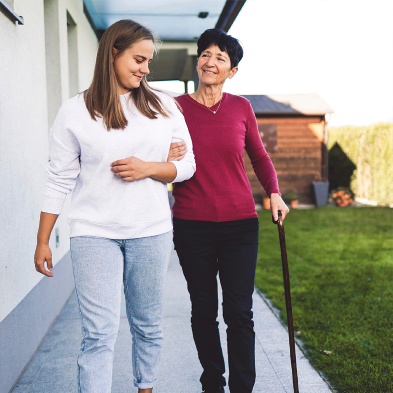 young woman helping older woman with a cane down the walkway